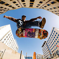 Man doing trick on a colorful skateboard with buildings behind him