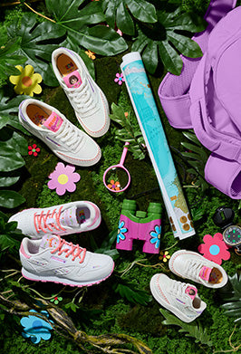 Three pairs of white sneakers with pink accents placed on various leaves with accessories like a magnifying glass and binoculars