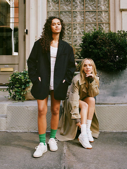 Two women wearing white sneakers standing outside building