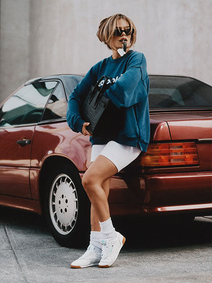 Woman in blue top and white sneakers leaning against a red car