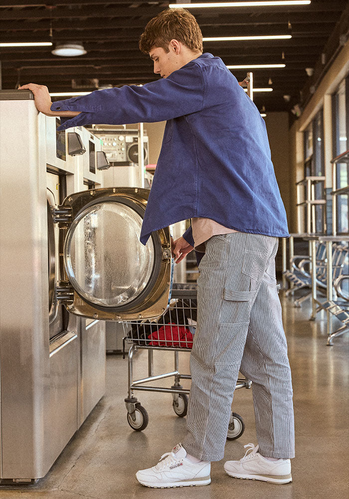 Man in blue top and gray pants wearing white sneakers doing laundry