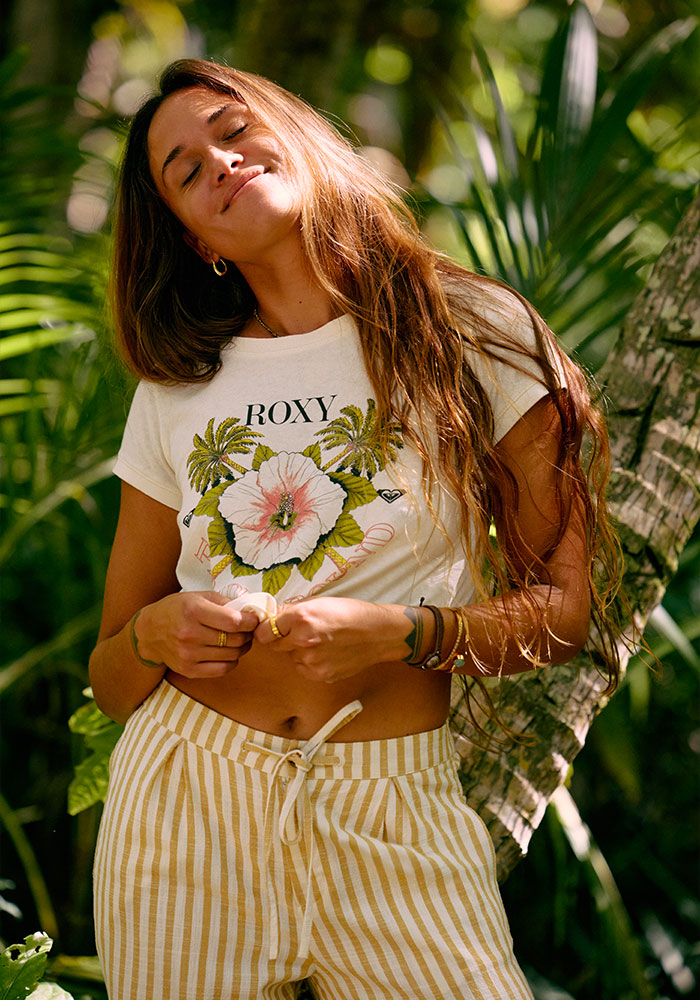 Woman in white floral-print shirt and striped pants standing amidst foliage