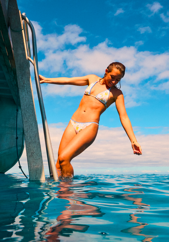 Girl in swimsuit hanging off boat and looking into water