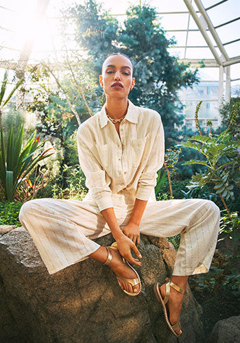 Woman in white outfit sitting on a rock in a greenhouse garden