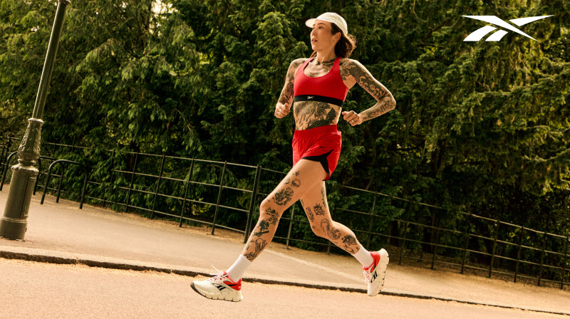 Person in red outfit and white and red sneakers running outside with white Reebok logomark in the top right