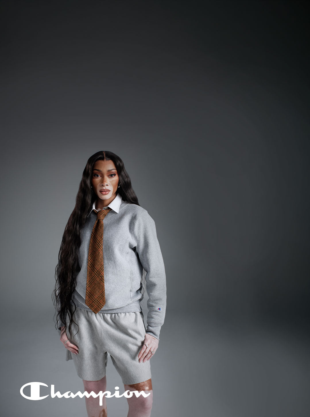 Woman in gray sweats and brown tie standing in gray studio background