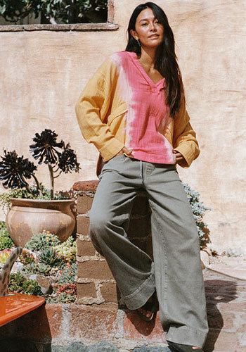 Woman posing in front of a building in a tie-dye top and loose green pants