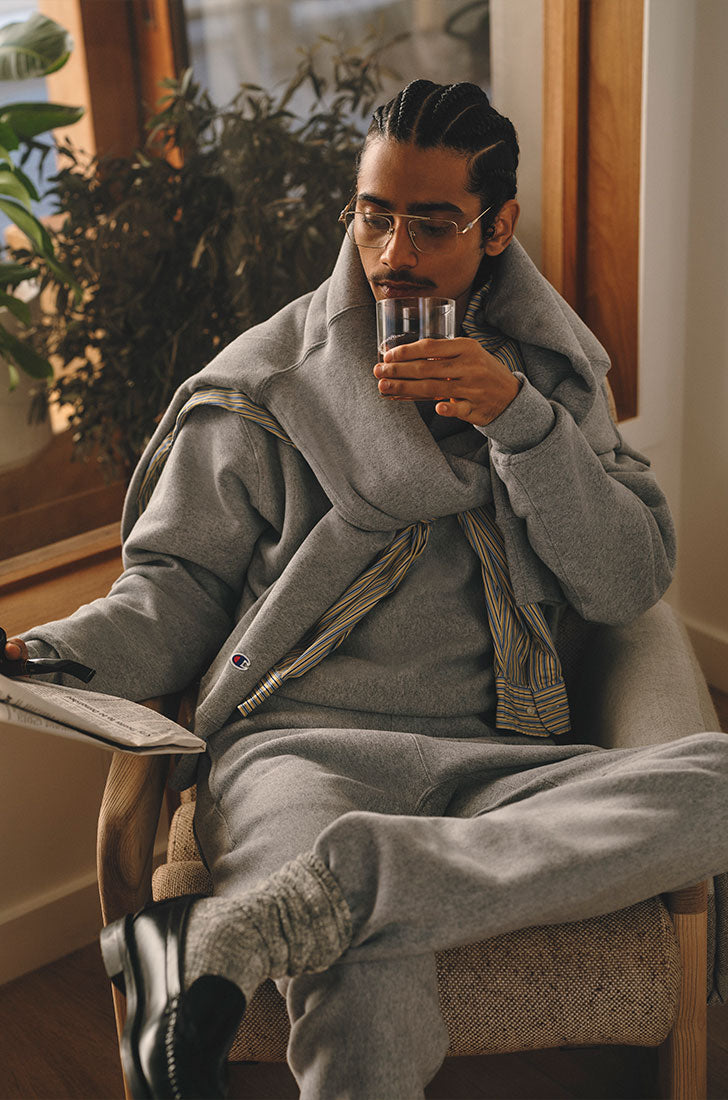 Man in grey sweats holding a glass and sitting indoors
